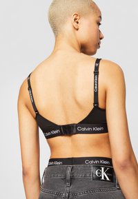 Svart bomull-bralette med logotrykte stropper, justerbart festesystem og en glatt tekstur. Matcher med svarte jeans med logo-linning.