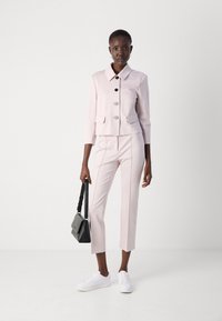 Lichtroze op maat gemaakte blazer met drie knopen en twee zakken, gecombineerd met bijpassende cropped broeken en witte sneakers. Zwart handtas in de hand.