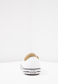 White canvas sneaker with a low-top design, black rubber sole, and "Converse All Star" branding on the heel. Simple and minimal texture.