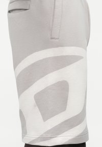 Sive kratke hlače iz mehkega bombaža z veliko belo abstraktno zasnovo. Imajo stranske žepke in raven kroj, ki se konča tik nad kolenom.