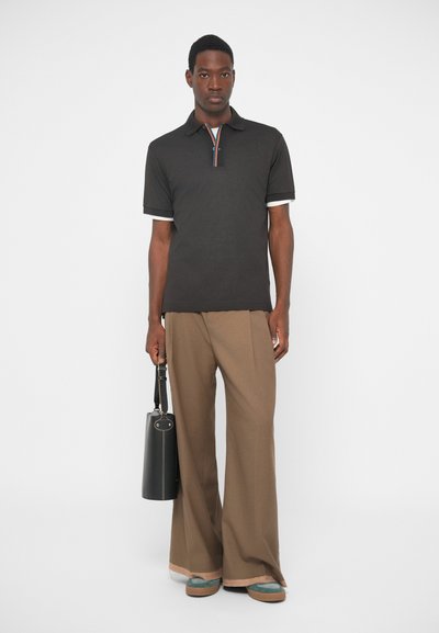 Μαύρο πόλο μπλουζάκι με κολάρο σε ρίγες, λευκά σορτσάκια στα μανίκια, σε συνδυασμό με καφέ παντελόνι φαρδύ και μαύρη τσάντα tote.