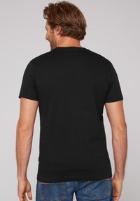 Camiseta de algodón negra de manga corta con cuello redondo y un sutil detalle del logo en la parte posterior, combinada con vaqueros de denim azul.