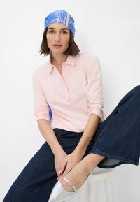 Lyserød langærmet polo-shirt med krave, parret med mørkeblå jeans og sølvfarvede flats. Blå og beige mønstret hovedscarf.