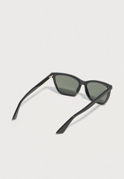 Μαύρα ορθογώνια γυαλιά ηλίου με σκούρους φακούς, ανοιχτά και τοποθετημένα πάνω σε λευκή επιφάνεια.