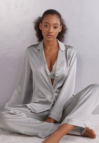 Pyjamaset i mjuk grå satin med en långärmad skjorta med knappar och matchande byxor, med delikat vit kant och avslappnad passform.