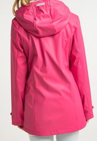 Giacca da pioggia impermeabile rosa con cappuccio, caratterizzata da una texture morbida, polsini regolabili e una lunghezza intermedia. Dettagli di cucitura chiara.