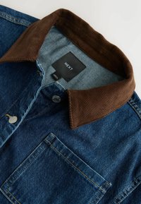 Veste en denim avec col en velours côtelé marron, boutons en métal, poche poitrine et étiquette en tissu noir avec l'inscription NEXT à l'intérieur du col.