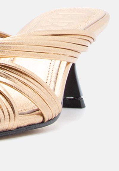 Bež sandala na visoku petu s crnim blok petom i teksturiranim uloškom na bijeloj pozadini.