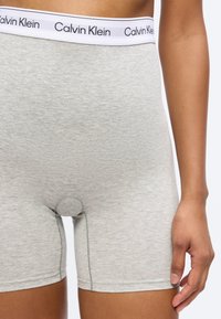 Κοντινή λήψη ενός ατόμου που φοράει ανοιχτό γκρι μποξεράκια με λευκή μέση με τη μάρκα "Calvin Klein".