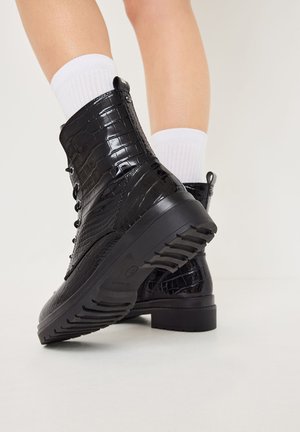 Bottines noires avec un revêtement brillant en cuir de crocodile, un laçage sur le devant et une semelle en caoutchouc texturée pour une meilleure adhérence.