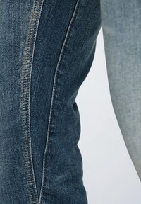 Vaqueros de mezclilla con un lavado en degradado de azul oscuro a claro, con un diseño ajustado y detalles de costura lateral. Se aprecia la textura de la tela.