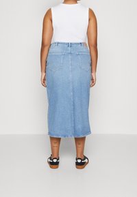 Denim midi kjol i ljusblått med rak skärning, två bakfickor och rå nederkant. Bärs med en vit ärmlös topp och svarta sandaler.