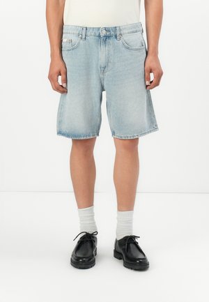 Shorts in denim azzurro chiaro con una vestibilità comoda, cinque tasche e orlo grezzo. Abbinati a calze bianche e scarpe nere con lacci.