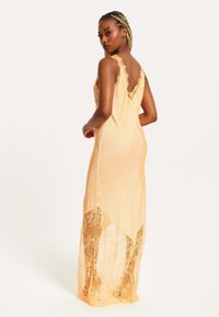 Peach-colored sleeveless dress with a lace trim at the hem and back, featuring a flowy design and sheer lace paneling.