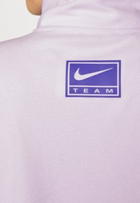Sudadera de forro polar morado con un alto cuello y un parche del logo de Nike en azul que dice "TEAM" en la parte posterior. Textura suave y diseño casual.