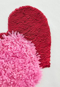 Cœur en sequins rouges avec un tissu texturé rose superposé présentant des formes ressemblant à des pétales ; les deux formes sont sur un fond blanc.