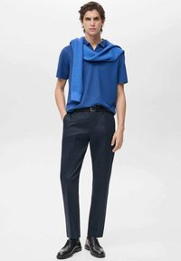 Sininen lyhythihainen polo-paita, joka on yhdistetty tummansinisiin mittatilauspö trousers. Yhteensopiva sininen neule on heitetty hartioille. Mustat juhlakengät viimeistelevät asun.