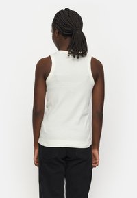 Weißes Baumwolltanktop mit kontrastierenden, gerippten Trägern, tailliertem Design und glatter Textur, kombiniert mit schwarzen Hosen, von hinten gesehen.