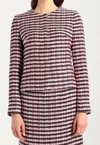 Meer-kleurig tweed jasje met een ronde halslijn, met een patroon van roze, zwart en witte ruiten. Lange mouwen en een knoopsluiting aan de voorkant.