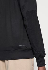 Zwarte DRI-FIT sweatshirt met gladde stof, textuurpanel op de manchette en geribbelde boorden. Minimalistisch ontwerp met subtiele branding.