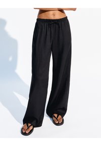 Black, loose-fitting pants made from lightweight fabric with an elastic waistband and drawstring. Paired with black flip-flops.