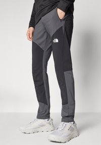Muške vanjske hlače u crnoj i tamnosivoj boji s taperiranim dizajnom. Sadrže zatvoreni džep i logo The North Face na donjem dijelu nogavice.
