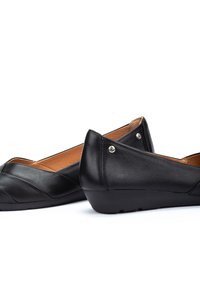 Bottines plates en cuir noir avec une texture lisse, bout pointu et couture décorative. Présente des accents en métal argenté sur le talon.