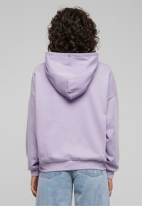 Sudadera de lavanda con capucha ajustable, hombros caídos y puños de canalé, combinada con jeans de tiro alto en un tono azul claro. Tejido suave y casual.
