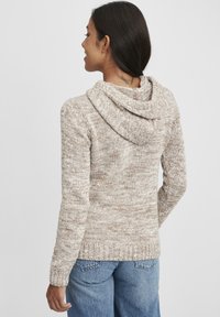 Beige strikket hettegenser med teksturert mønster, lange ermer og en avslappet passform. Har søm bak på nakken og ribbestrikkede mansjetter og hem.