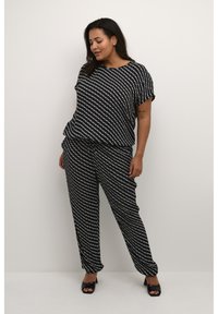 Completo bianco e nero a due pezzi con top dalla vestibilità ampia e pantaloni aderenti con vita elastica. Indossato con scarpe nere con punta aperta.