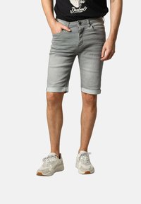 Shorts en denim gris, ajustés avec des revers, et des poches avant. Portés avec un T-shirt noir et des baskets blanches à détails texturés.