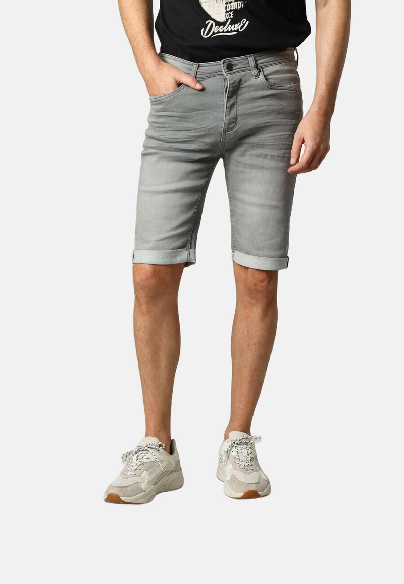Shorts en denim gris, ajustés avec des revers, et des poches avant. Portés avec un T-shirt noir et des baskets blanches à détails texturés.