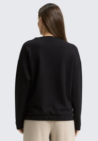 Pull noir à manches longues avec une texture côtelée, coupe décontractée et ourlet inférieur élastiqué. Le matériau semble doux et confortable.