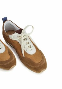 Sneaker in suede marrone con dettagli in pelle bianca, punta rotonda, lacci crema e un tassello blu sul tallone. Superficie testurizzata con dettagli cuciti.