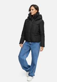 Black puffer jacket with a hood, featuring a zip closure and two front pockets. Worn with blue wide-leg jeans and white sneakers.