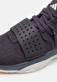Gros plan d'une chaussure de sport noire avec une large bride perforée au-dessus des lacets et une semelle blanche texturée.