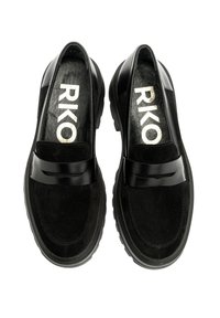 Un paio di mocassini in pelle e suede nera con suole spesse, dotati di strap lucidi e con "RIKO" stampato in oro all'interno di ogni scarpa.