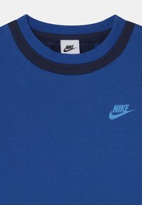 Camiseta azul de Nike con ribete de color azul más oscuro en el cuello y logo de Nike en azul claro en el lado izquierdo del pecho.