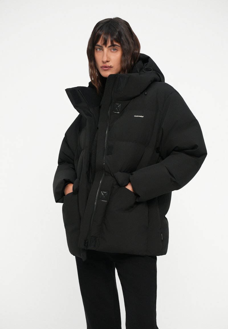 Doudoune noire avec capuche, dotée d'une fermeture éclair, de grandes poches avant et d'accents texturés. Coupe légèrement oversize et design matelassé.