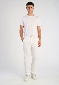 Witte t-shirt en witte broek op een persoon. De katoenen stof heeft een gladde textuur. Witte sneakers maken de outfit compleet. Neutrale achtergrond.