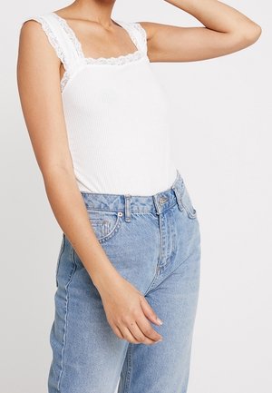 Wit geribd tanktopje met een vierkante halslijn afgezet met kant, gecombineerd met hoogwater lichtblauwe denim jeans. Natuurlijke stoftextuur.