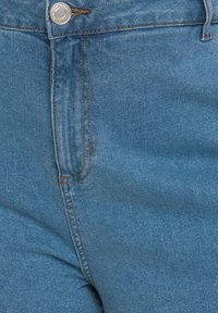 Jeans de mezclilla azul con una textura suave, que presentan costuras en contraste y un detalle de botón plateado en la cintura. Vista en primer plano de la tela.