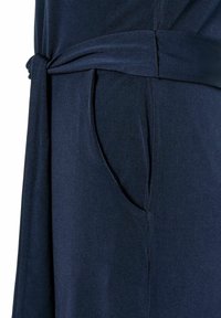 Dunkelblaues Kleid mit einer Seitentasche und einem geknoteten Gürteldetail. Hergestellt aus weichem Stoff mit glatter Textur und minimalistischem Design.