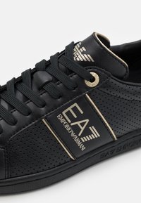 Svarta lädersneakers med perforeringar, svarta snörningar och guld Emporio Armani EA7-logotyp på sidan och tungan.