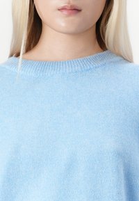 Kročnik osebe z nižjega obraza in vratu, oblečeno v svetlo modro pleteno majico in z dolgimi blond lasmi.