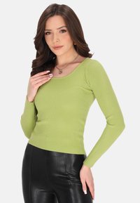 Grünes, geripptes Langarmshirt mit rundem Halsausschnitt. Kombiniert mit schwarzen, enganliegenden Hosen, die die Textur des Shirts betonen. Schlichte Designelemente.