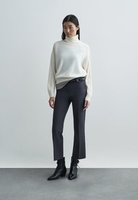 Kremasta rolka uparena sa crnim uskim hlačama i crnim gležnjačama. Džemper ima rebraste detalje i spuštene ramene šavove.