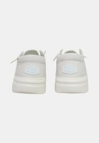 Zapatillas de lona blancas con una superficie texturizada, marca azul claro y suela blanca gruesa; cuentan con cordones y pequeñas lengüetas.