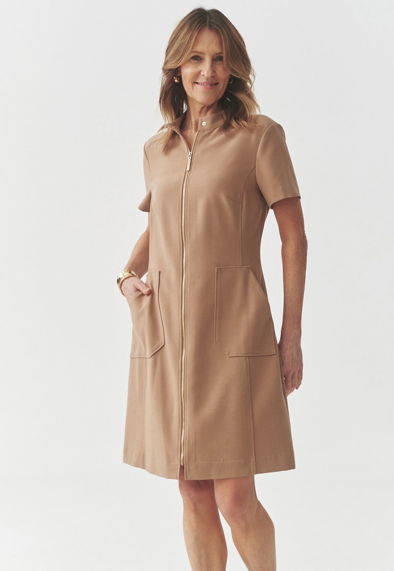 Ein braunes Kleid aus einem glatten Stoff, mit kurzen Ärmeln, einem Reißverschluss vorne und zwei rechteckigen Vorderstaschen.