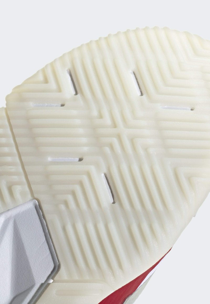 Suela de zapato en goma blanca con un patrón de espiga. El borde presenta un acento rojo y una superficie texturizada con ranuras y muescas.